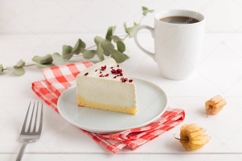 Piece of cheesecake on gray plate on kitchen spatula and cup of coffee on background