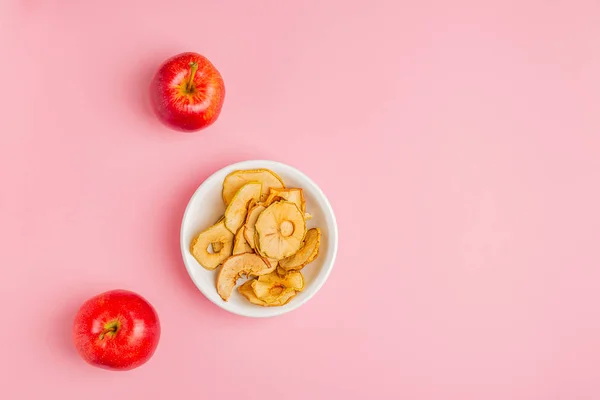 Dried apples chips in ceramic bowl with fresh red apples on table
