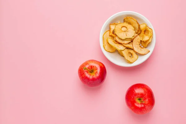 Dried apples chips in ceramic bowl with fresh red apples on table