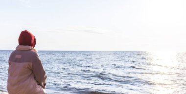 Bir akşamın arka planında bir bankta oturan kız gün batımına bakar suya.