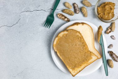 Beyaz masada yeşil plastik bıçağın yanında fındıklı tost ekmeği üzerine fıstık ezmesi.