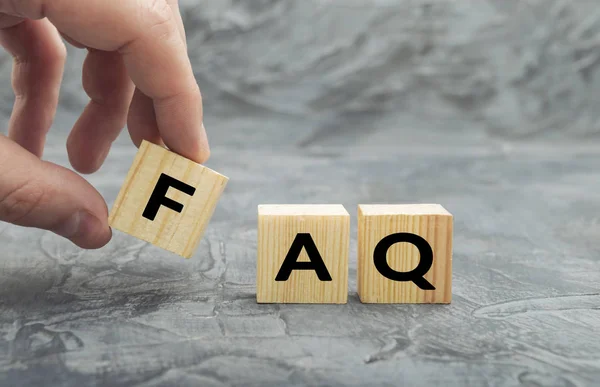 Hand putting wooden cube block with word FAQ  (frequently asked