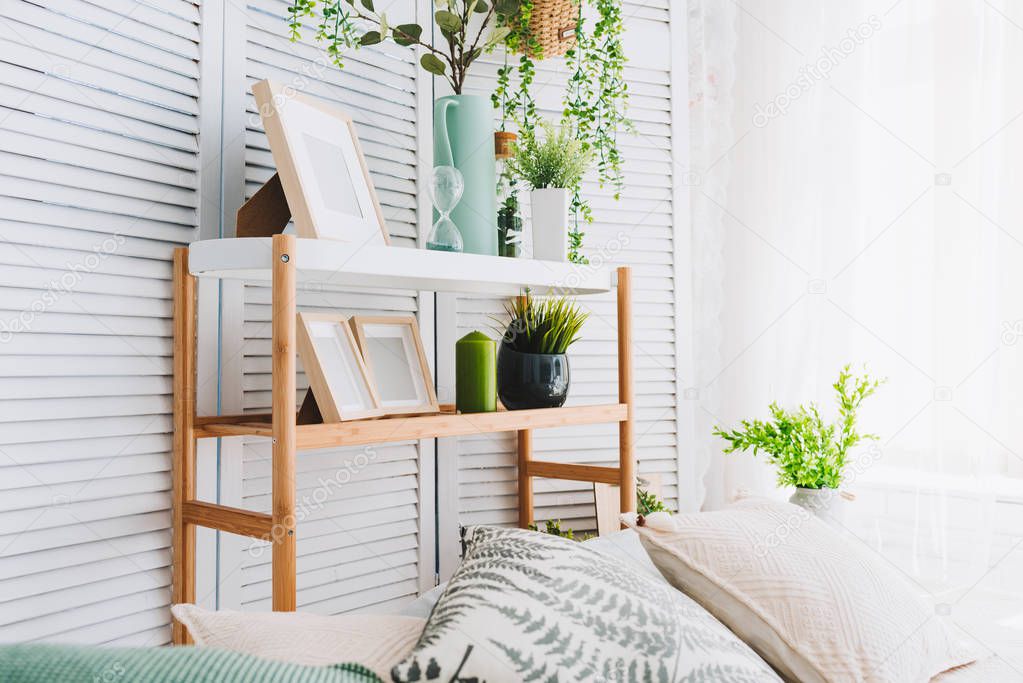 Cozy brightly lit room corner decorated with various objects such as picture frames, plants and pillows