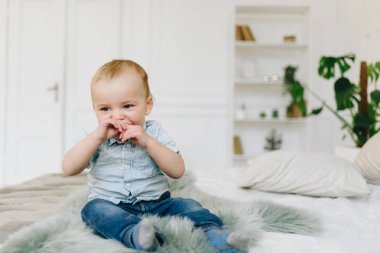 Sevimli küçük yürümeye başlayan çocuk kot pantolon ve gömlek giyen yatakta oturan