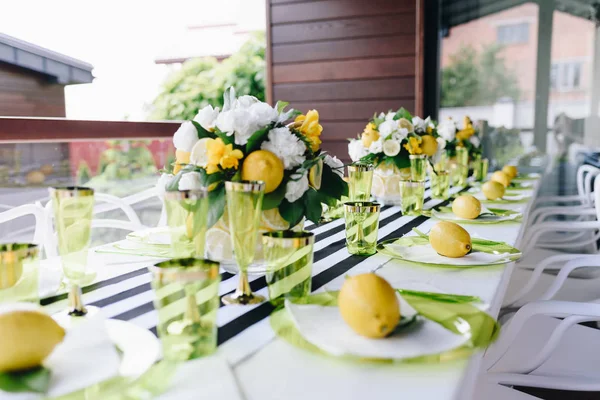 Ένα εορταστικό τραπέζι σερβίρεται με πράσινα γυάλινα σκεύη διακοσμημένα με ολόκληρα λεμόνια και μπουκέτο λουλουδιών — Φωτογραφία Αρχείου