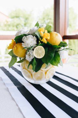 Çizgili masa örtüsü ile bir masada taze sarı ve beyaz çiçek ve limon yaratıcı bir buket