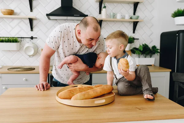 Unga kaukasiska far pratar med sin son och hålla ett barn i köket — Stockfoto