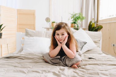 Sevimli bir beyaz kız ellerini yüzünü eğilerek yatakta oturan