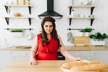 Üzerinde baget olan mutfak masasında oturan kırmızı elbiseli genç ve güzel bir kadın.