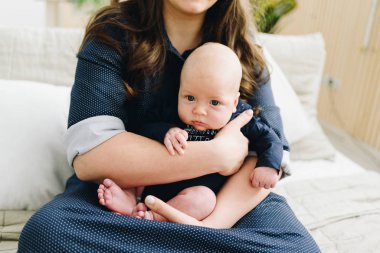 Annesinin kollarında oturan beyaz bir bebek. 