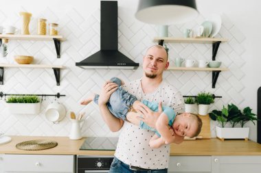 Mutfakta onunla oynarken küçük oğlunu tutan genç ve sağlıklı bir adam.