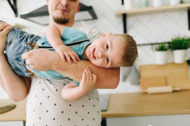 Babasının kollarında küçük bir gülen çocuk mutfakta oynuyor.
