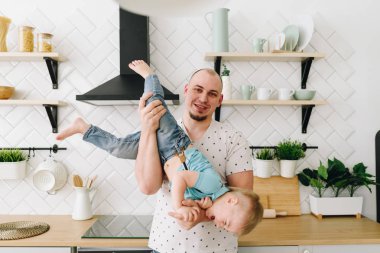 Genç bir baba hafif bir mutfakta oğlunu başını aşağı tutarak 