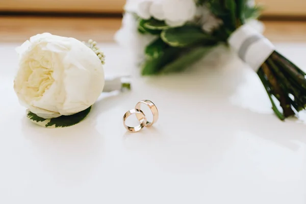 Close-up boutonniere com anéis de casamento dourados e um buquê no fundo — Fotografia de Stock