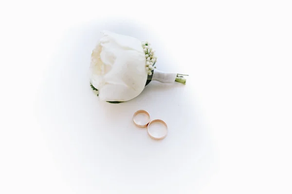 A top-down lay flat boutonniere com anéis de casamento no fundo branco — Fotografia de Stock