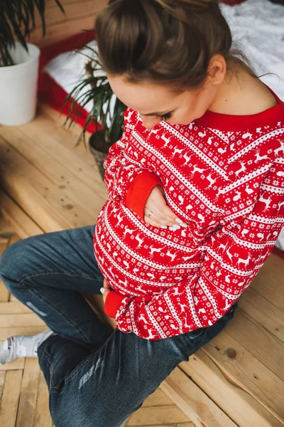 Mulher grávida vestindo camisola de Natal sentado e olhando para sua barriga de cima para baixo — Fotografia de Stock