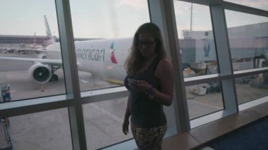 Gidiş salonunda cep telefonu kullanan genç kadın. Ağustos 2016 arka planda, Charlotte, North Carolina, ABD, American Airlines şirketi bir uçaktan mı