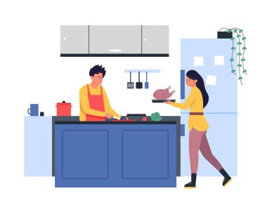 Young smiling man and woman are cooking together in a domestic kitchen, he s cutting vegetables while she s holding a plate with a whole roasted turkey