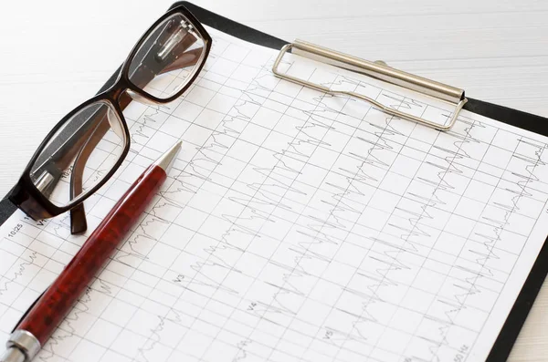 Electrocardiogram graph, heart analysis. Black clipboard, ballpoint pen, glasses