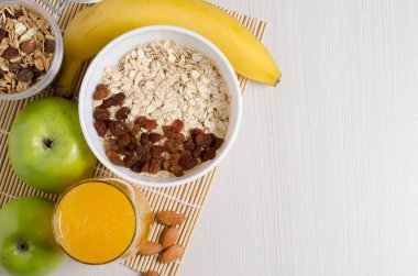 Bambu dan masa örtüsü üzerinde üzümlü yulaf ezmesi. Portakal suyu, meyve, badem. Düz üstten görünüm