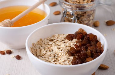 Sağlıklı kahvaltı. Beyaz kase kuru üzümlü yulaf ezmesi. Badem, beyaz masa arka plan üzerinde tatlım. Yan görünüm