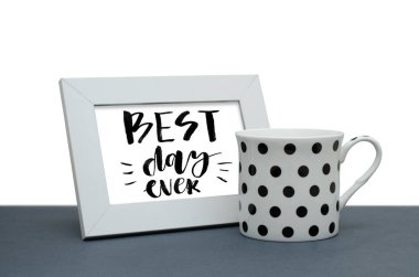 Şimdiye kadar en güzel günü. El yazısı metnini, ilham alıntı olduğunu. Modern hat. Beyaz ahşap çerçeve. Masada beyaz kahve fincanı. Yakın çekim, beyaz arka plan