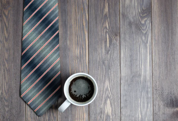 Erkekler kravat ve ahşap arka plan üzerinde beyaz bir fincan kahve. Düz top vie
