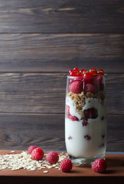 Sağlıklı kahvaltı. Tatlı bir cam-yoğurt, yulaf ezmesi, ahududu, kırmızı frenk üzümü. Ahşap arka plan. Yan görünümü. Uzay kopyalayın. Dikey fotoğraf