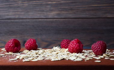 Kırmızı ahududu ve kahverengi bir kesme tahtası üzerinde yulaf ezmesi. Kopya alanı