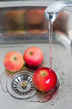 Gıda hijyeni. Metal bir lavaboda su akışı altında üç kırmızı elma. Dikey fotoğraf