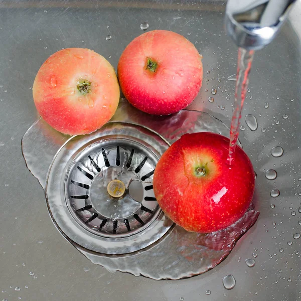 Gıda hijyeni. Metal bir lavaboda su akışı altında üç kırmızı elma