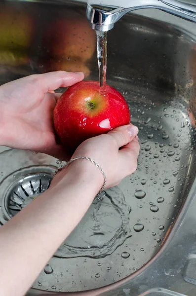 Food hygiene. Red apple with water splash on hands. Vertical photo