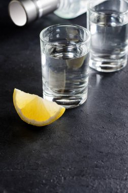 Koyu gri arka plan, limon parçası, bir şişe votka votka bardak. Uzay kopyalayın. Dikey fotoğraf