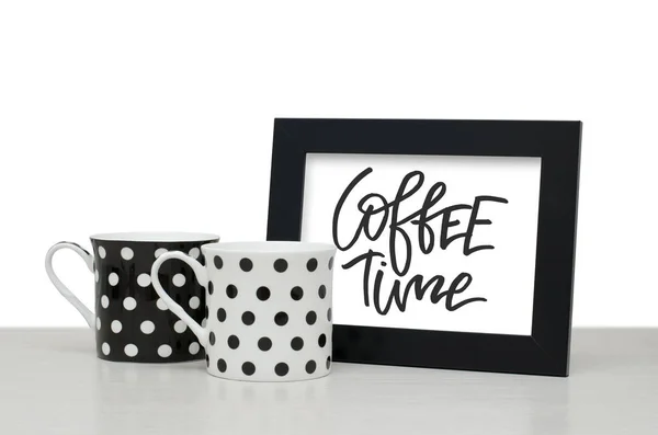 Coffee time. Handwritten text. Modern calligraphy. Black wooden frame for text. Black and white coffee Cup on the table. Close-up, white background