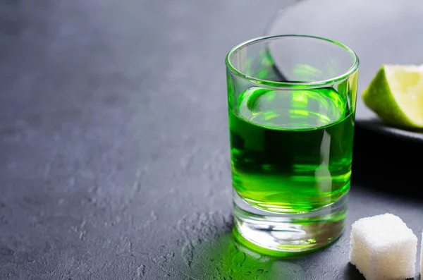 Absinthe green liquor in glasses. Alcoholic hallucinogenic beverage. Dark background. Pieces of lime and white sugar. Copy space