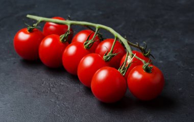 Yeşil bir dalda olgun kırmızı domates. Vitamin açısından zengin sebzeler. Koyu arka plan.