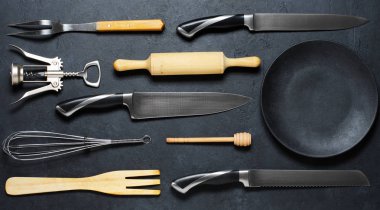 Ahşap ve metal mutfak gereçleri ve siyah bir tabak . Yemek pişirmek için aletler. Karanlık arka plan. Düz yatıyordu