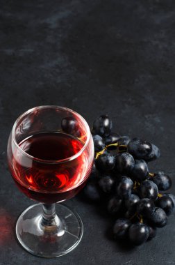 Bardakta kırmızı şarap, bir demet üzüm. Karanlık arka plan. Kopyalama alanı
