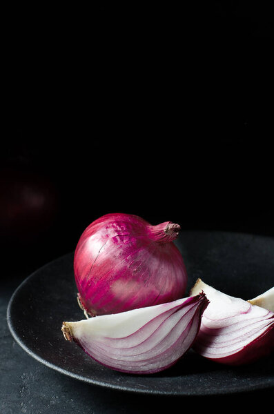 Red onion. Large onion and sliced on a black plate. Black background. Side view. Red onions on old crumpled burlap. Copy space.