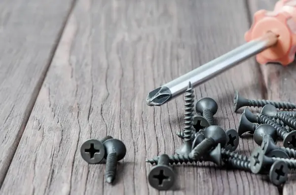 Tornillos de metal y un destornillador sobre un fondo de madera. Herramienta de fijación y reparación. Copiar espacio — Foto de Stock