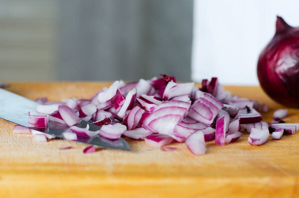 Красный лук нарезан. Процесс приготовления на желтой разделочной доске. Селективный фокус
