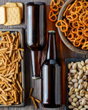 Cam şişelerde bira ve ahşap tabaklarda bira için tuzlu atıştırmalıklar. Kırsal tarzda. Kahverengi ahşap arka plan