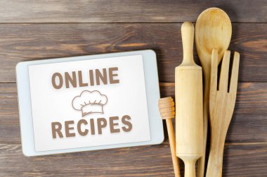 İnternette tarifler. Tablet bilgisayarda yemek kitabı. Mutfak aletleri. Kahverengi ahşap arka plan.