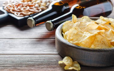 Bira şişelerinde bira ve bira için tuzlu atıştırmalıklar. Kahverengi ahşap arka plan. Arkadaşlar için bir parti konsepti. Boşluğu kopyala