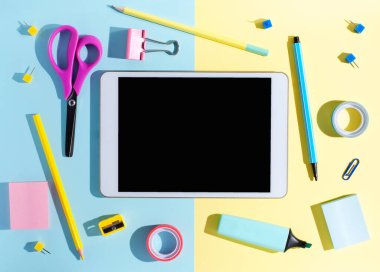 Boş ekranlı bir tablet ve renkli bir arka planda ofis malzemeleri. Okul çocukları için konsept uygulama ya da çocuklar için çevrimiçi öğrenme. Boşluğu kopyala.