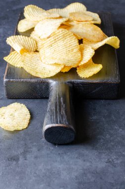 Siyah tahta kesme tahtasında tuzlu cips. Koyu beton arka plan. Bira çerezi. Boşluğu kopyala