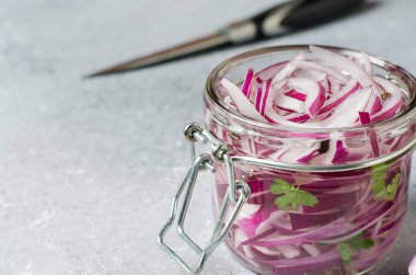 Cam bir kavanozda sirkede doğranmış kırmızı soğan turşusu. Et ve balık yemekleri için lezzetli bir meze. Açık gri arkaplan.