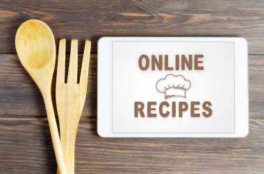 İnternette tarifler. Tablet bilgisayarda yemek kitabı. Mutfak aletleri. Kahverengi ahşap arka plan.