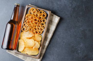 Koyu cam şişelerde bira ve tuzlu atıştırmalıklar. Koyu beton arka plan. Üst Manzara. Metin için boş alan