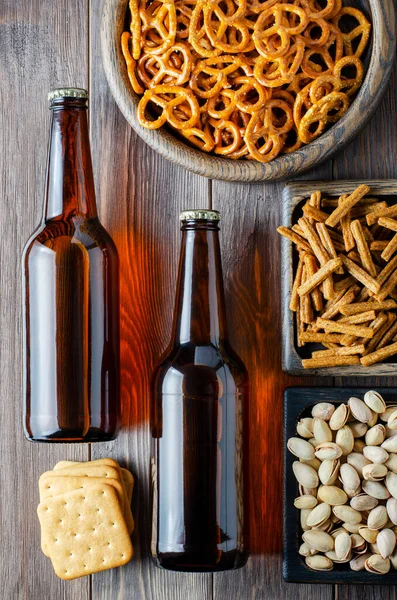 Beer in glass bottles and salty snacks for beer in wooden dishes. Rustic style. Brown wooden background